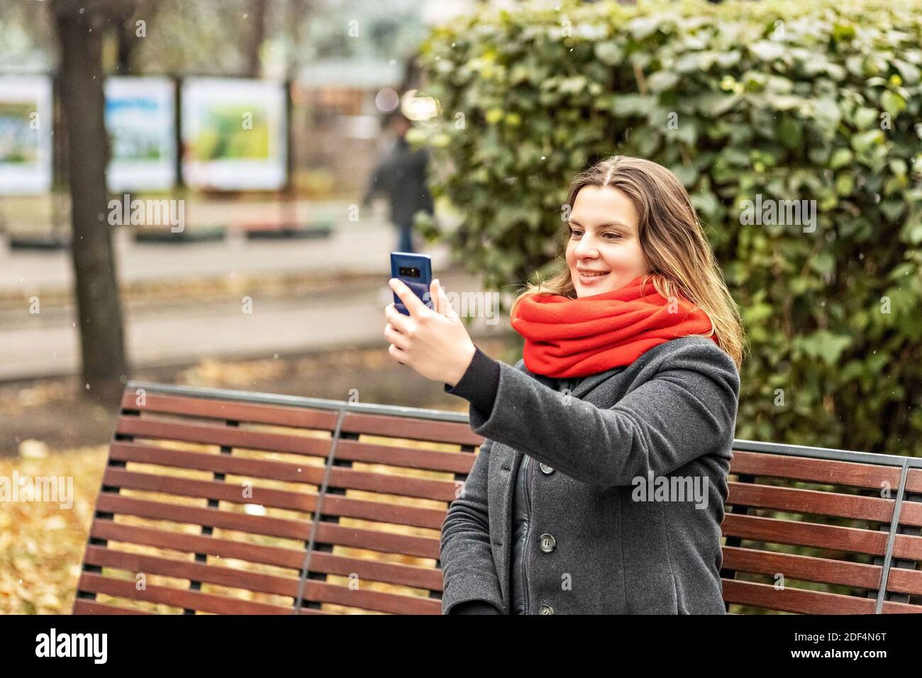 Junge lächelnde Frau Videochat mit dem Smartphone auf einer Parkbank sitzend. Videoanruf an ein Mobiltelefon. Das Mädchen spricht. Video-Chat in sozialen Netzwerken Stockfoto