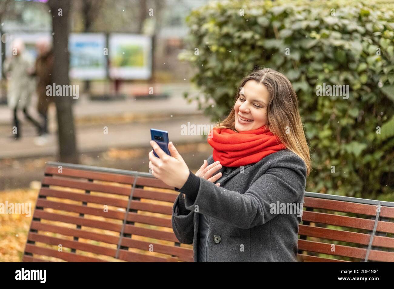 Junge lächelnde Frau Videochat mit dem Smartphone auf einer Parkbank sitzend. Videoanruf an ein Mobiltelefon. Das Mädchen spricht. Video-Chat in sozialen Netzwerken Stockfoto