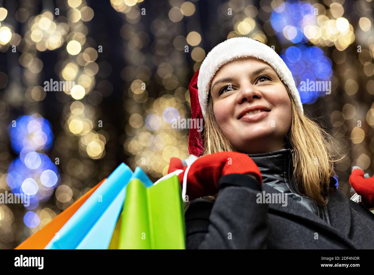 Eine Frau mit langen Haaren und einem Weihnachtsmütze am Fenster eines Stadtladens mit Einkäufen in bunten Papiertüten. Einkaufen im neuen Jahr. Stockfoto