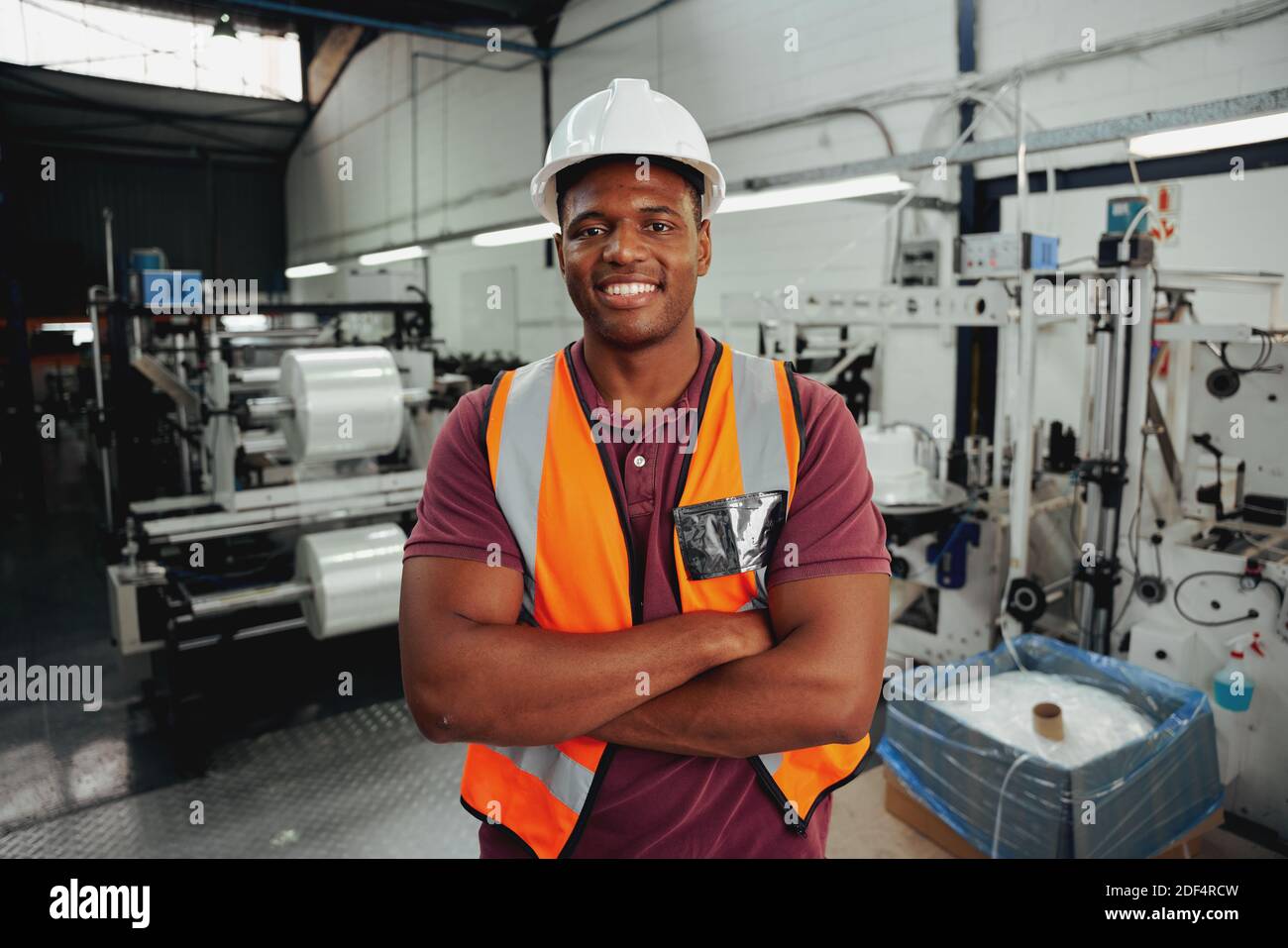 Fröhlich zuversichtlich junge afrikanische männliche Industriearbeiter Blick auf Kamera Mit gekreuzten Armen Stockfoto