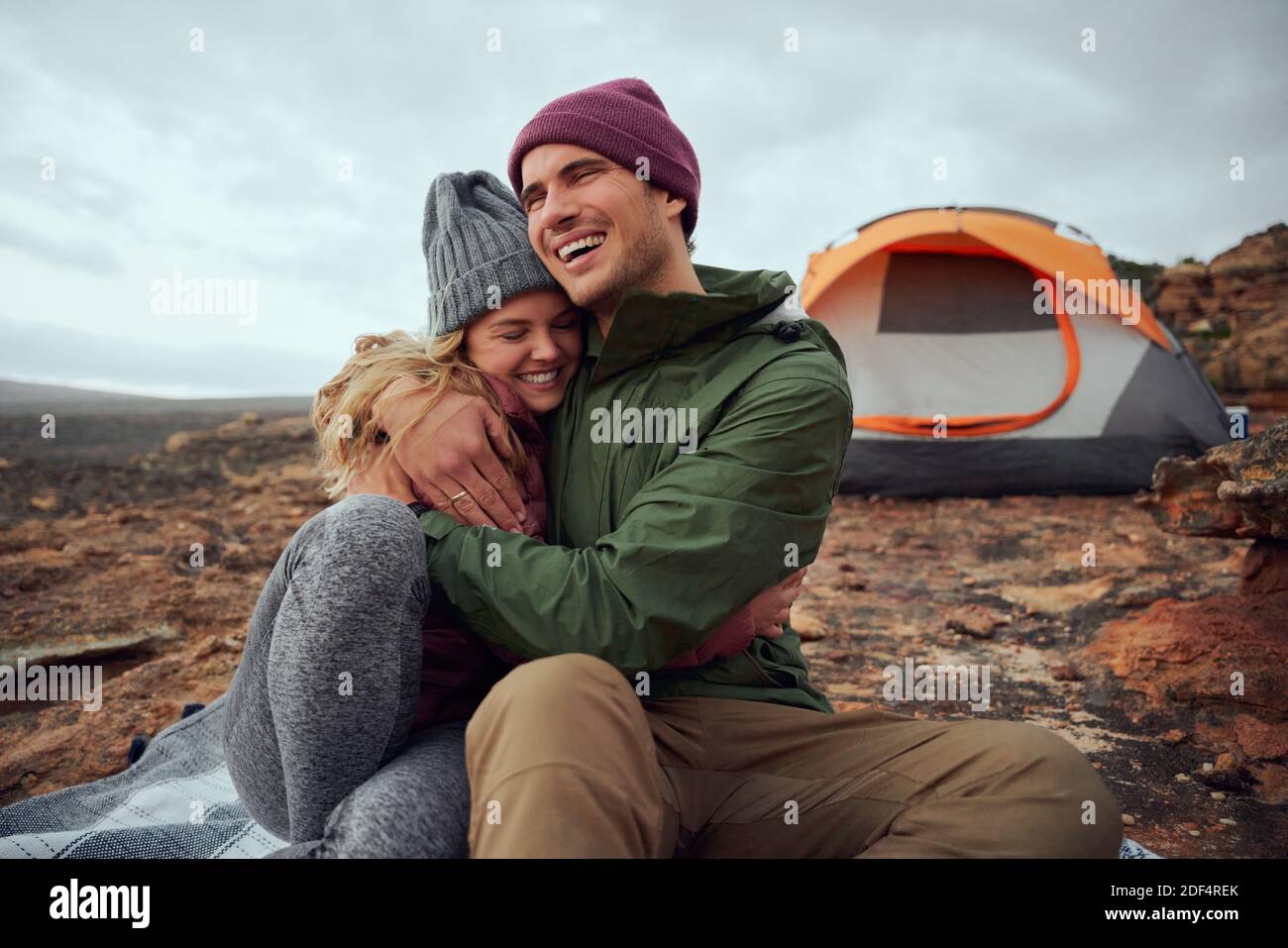 Glücklicher junger Mann umarmt seine lächelnde Freundin und schaut weg Während des Campens Stockfoto