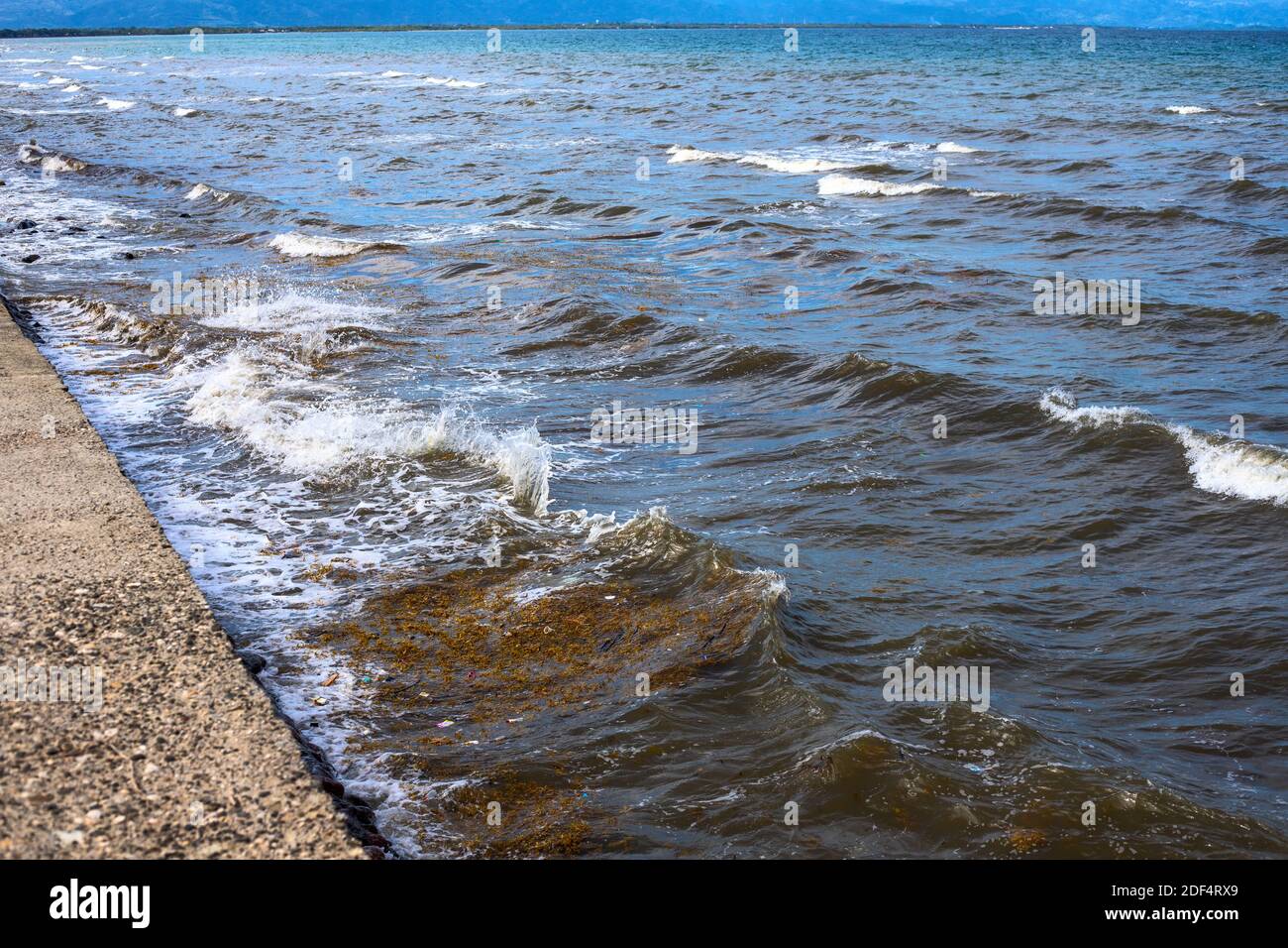 Meerwasser mit Wellen, Algen und Müll. Wasserabfall in der Nähe der städtischen Böschung. Asiatische Stadt ozeanische Verschmutzung. Plastikmüll im Meer. Verschmutztes Meer Vie Stockfoto