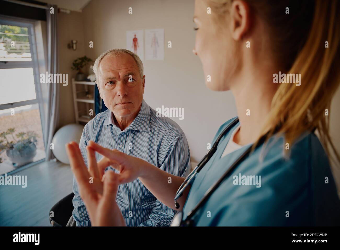 Fokussierter älterer männlicher Patient, der jungen Physiotherapeuten zuhört, die über erklären Behandlung in der Klinik Stockfoto