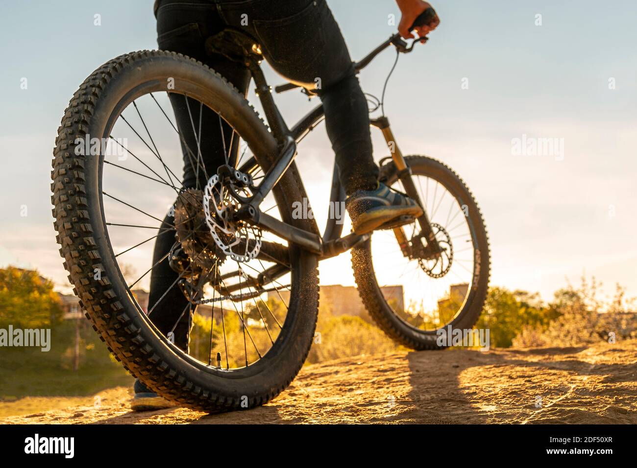 Mann auf dem Mountainbike. Fahrrad Räder Nahaufnahme Bild auf Sonnenuntergang. Niedriger Winkel Ansicht des Radfahrers Mountainbike. Fuß auf Pedal. Stockfoto
