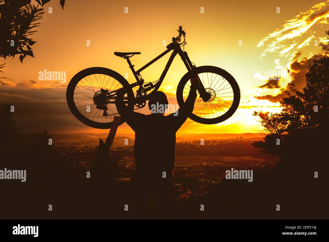 Silhouette eines Mountainbiker, der bei Sonnenuntergang ein Fahrrad über dem Kopf hält. MTB, Enduro, Freeride Hintergrund. Stockfoto