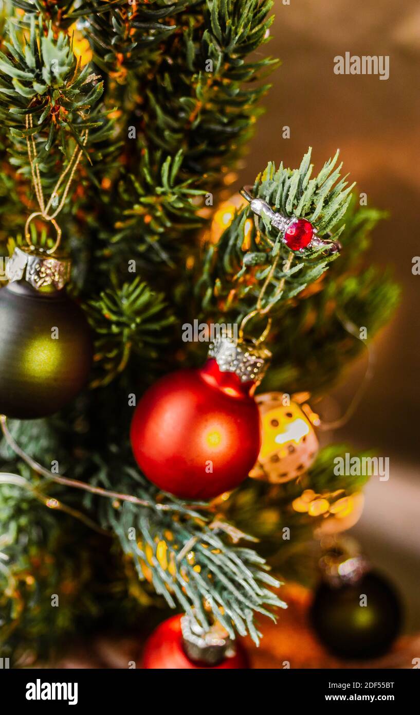 Silberner Verlobungsring mit rotem Rubin auf einem Zweig von geschmückten Weihnachtsbaum. Stockfoto