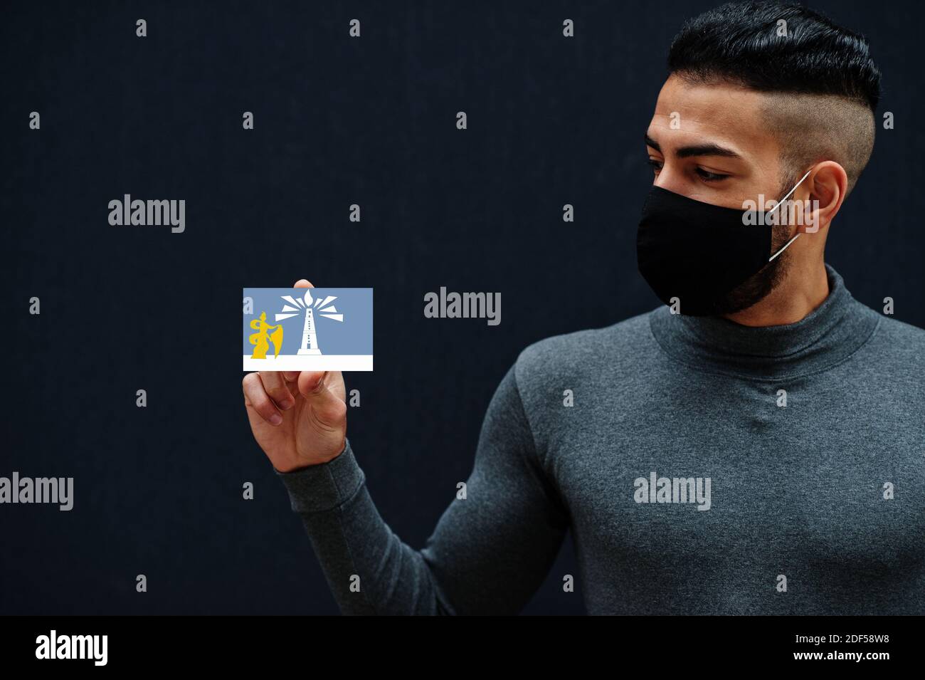 Ägyptischer Mann in grau Rollkragen und schwarz Gesicht schützen Maske zeigen Alexandria Flagge isoliert Hintergrund. Gouvernements von Ägypten Coronavirus Konzept. Stockfoto