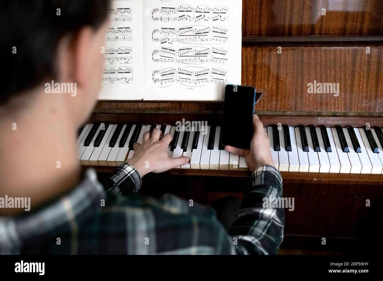 Lehrer hält sein Telefon während seiner Online-Klavierstunde Stockfoto