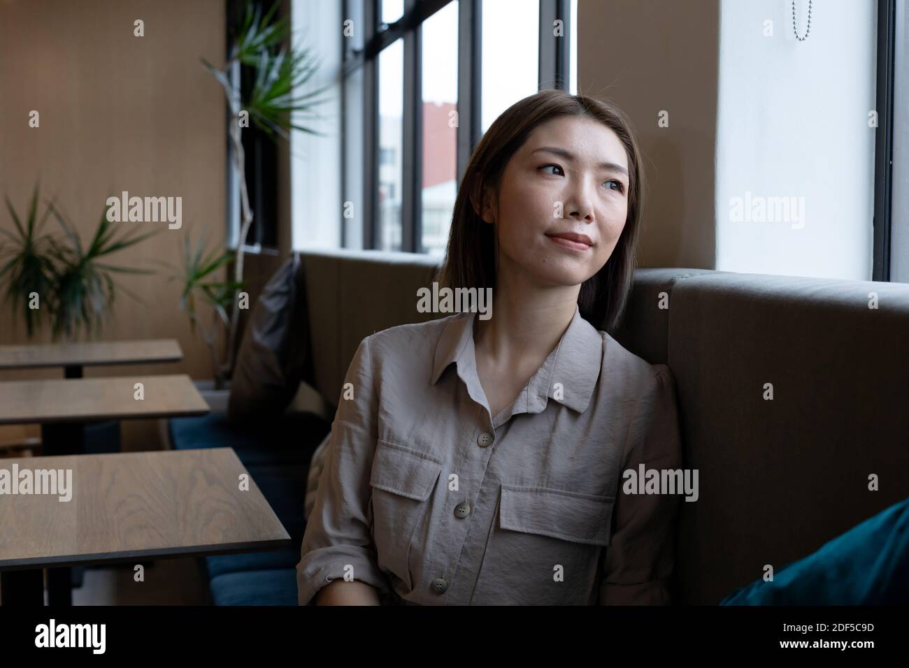 Asiatische Frau, die aus dem Fenster in der kreativen Bürokantine schaut Stockfoto