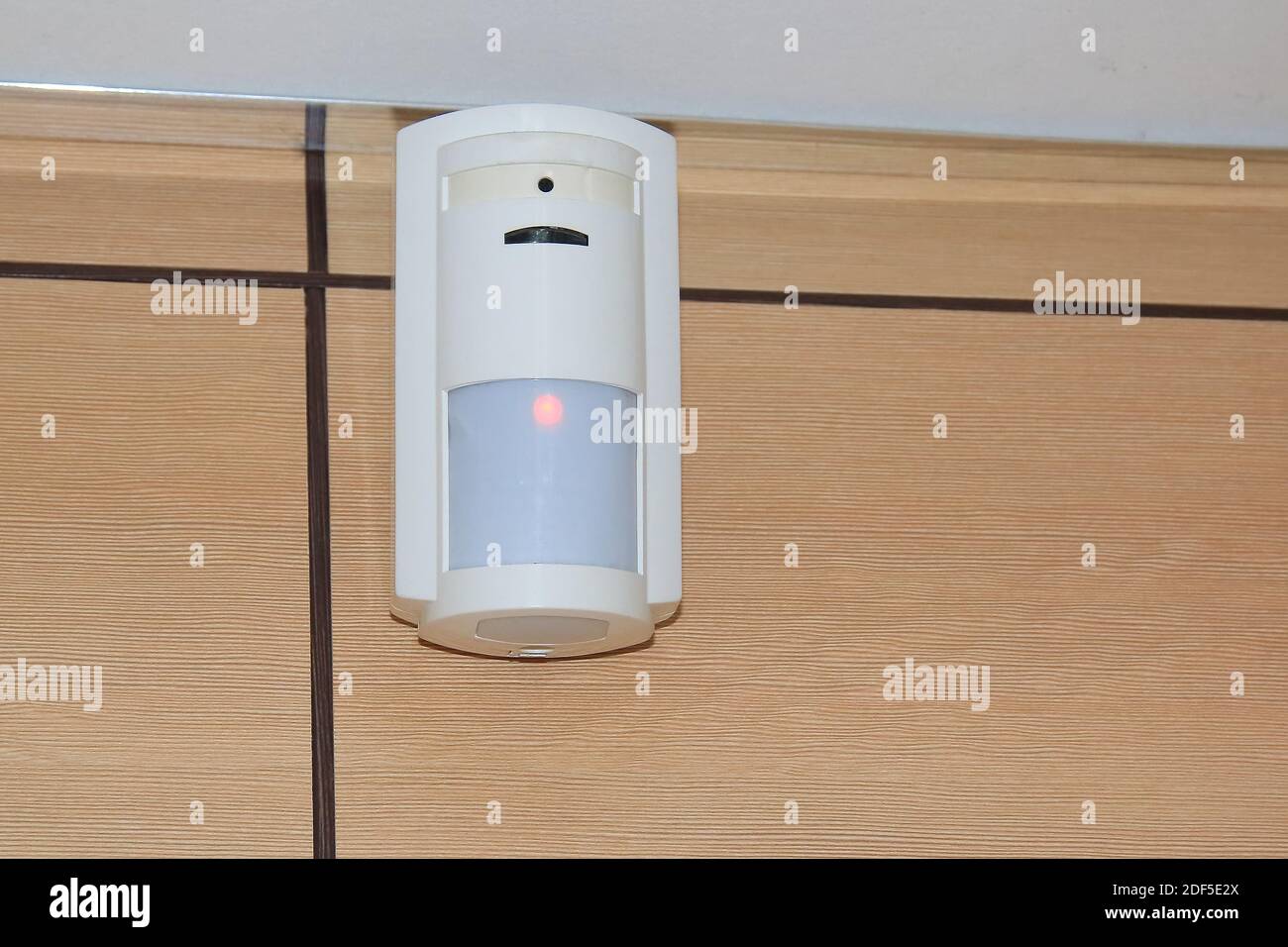 Bewegungssensor der Alarmanlage. In einem Raum oder Büro hängt ein weißer Volumensensor an der Wand. Stockfoto