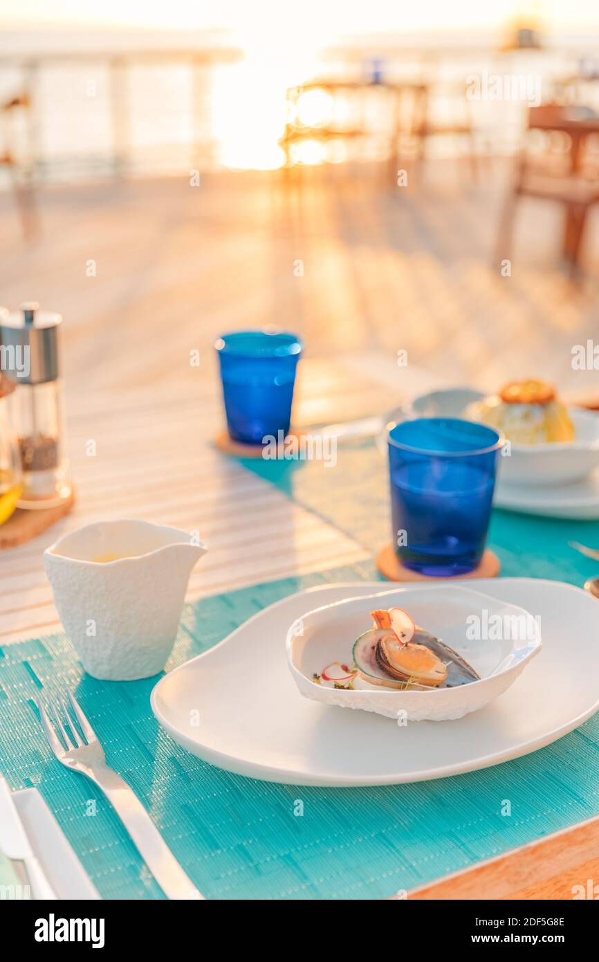 Tolles romantisches Abendessen am Strand auf der Holzterrasse mit Kerzen unter dem Sonnenuntergangshimmel. Romantik und Liebe, Luxus-Destination Dining, exotische Tisch-Setup Stockfoto