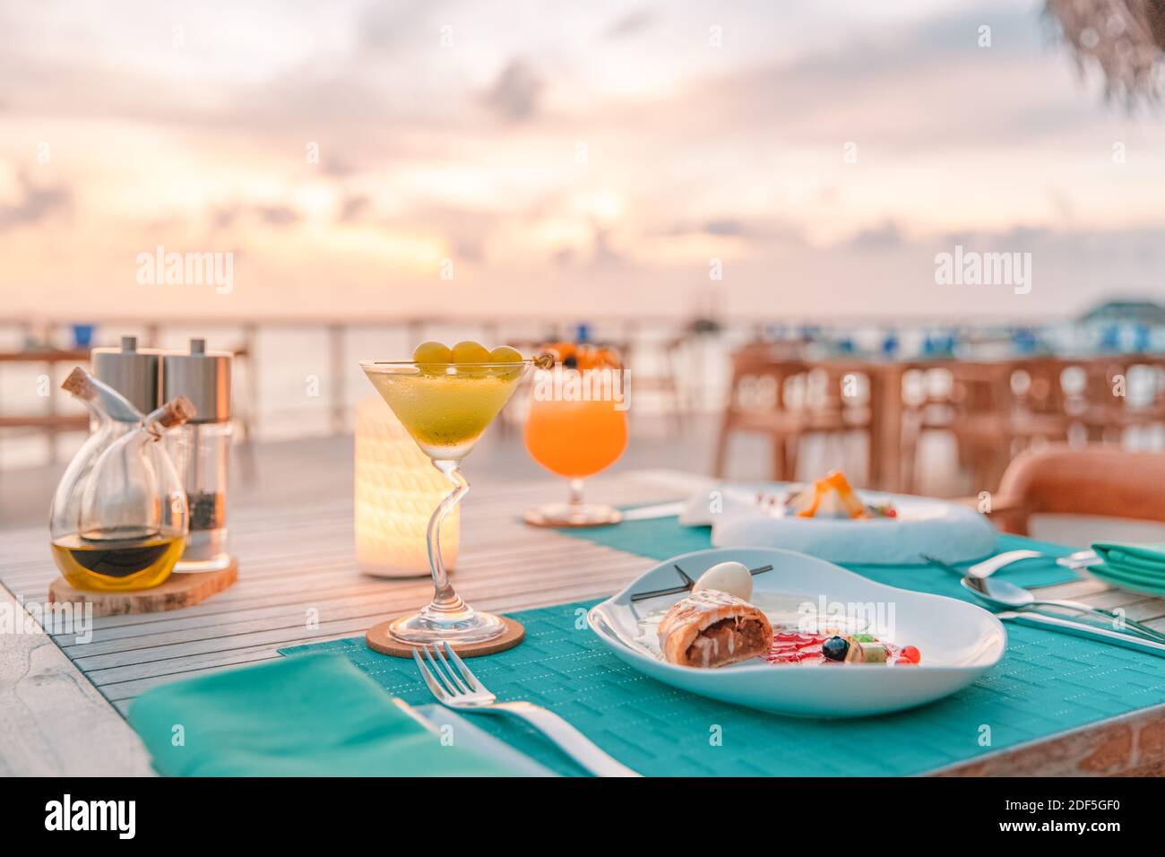 Tolles romantisches Abendessen am Strand auf der Holzterrasse mit Kerzen unter dem Sonnenuntergangshimmel. Romantik und Liebe, Luxus-Destination Dining, exotische Tisch-Setup Stockfoto