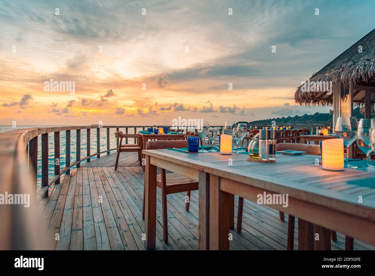Tolles romantisches Abendessen am Strand auf der Holzterrasse mit Kerzen unter dem Sonnenuntergangshimmel. Romantik und Liebe, Luxus-Destination Dining, exotische Tisch-Setup Stockfoto