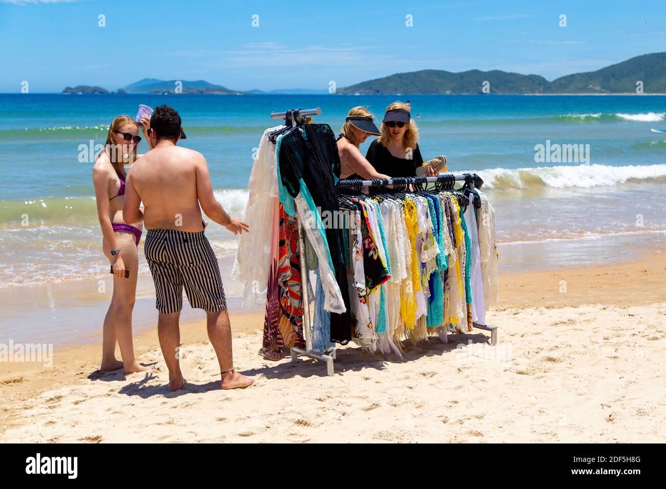 Geriba Beach, Buzios, Rio de Janeiro, Brasilien - 22. Dezember 2019: Menschen rund um den Kleiderständer eines Strandverkäufers. Mit bunten Kleidern. Stockfoto