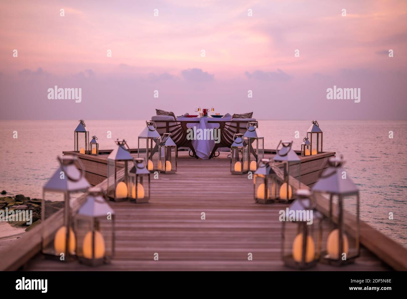 Toller romantischer Strand zum Abendessen auf einer Holzterrasse mit Kerzen unter dem Sonnenuntergang. Romantik Liebe, Luxus Destination Dining, exotische Tisch Setup, Meerblick Stockfoto