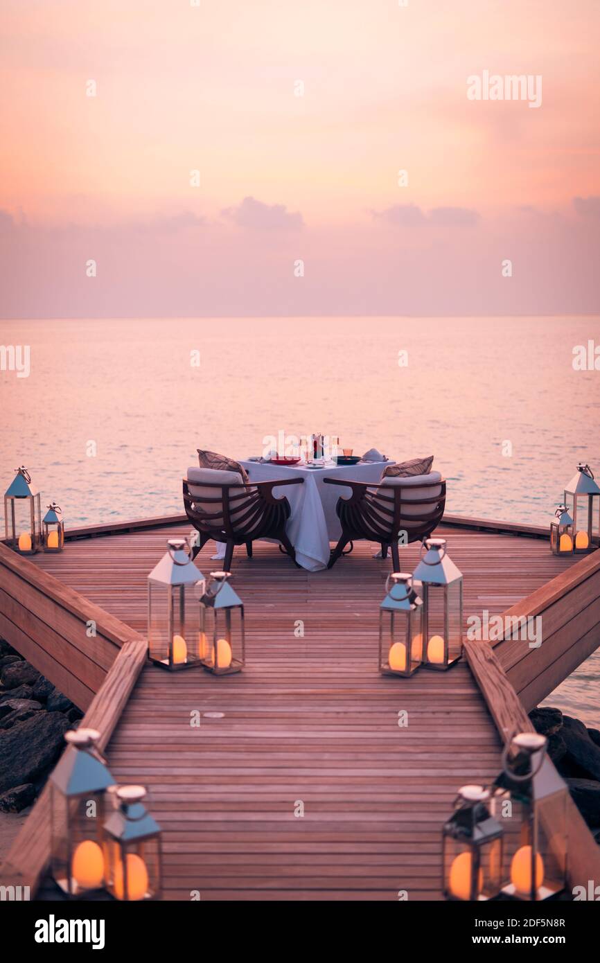 Toller romantischer Strand zum Abendessen auf einer Holzterrasse mit Kerzen unter dem Sonnenuntergang. Romantik Liebe, Luxus Destination Dining, exotische Tisch Setup, Meerblick Stockfoto