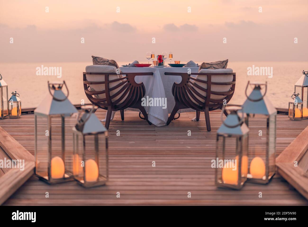 Toller romantischer Strand zum Abendessen auf einer Holzterrasse mit Kerzen unter dem Sonnenuntergang. Romantik Liebe, Luxus Destination Dining, exotische Tisch Setup, Meerblick Stockfoto