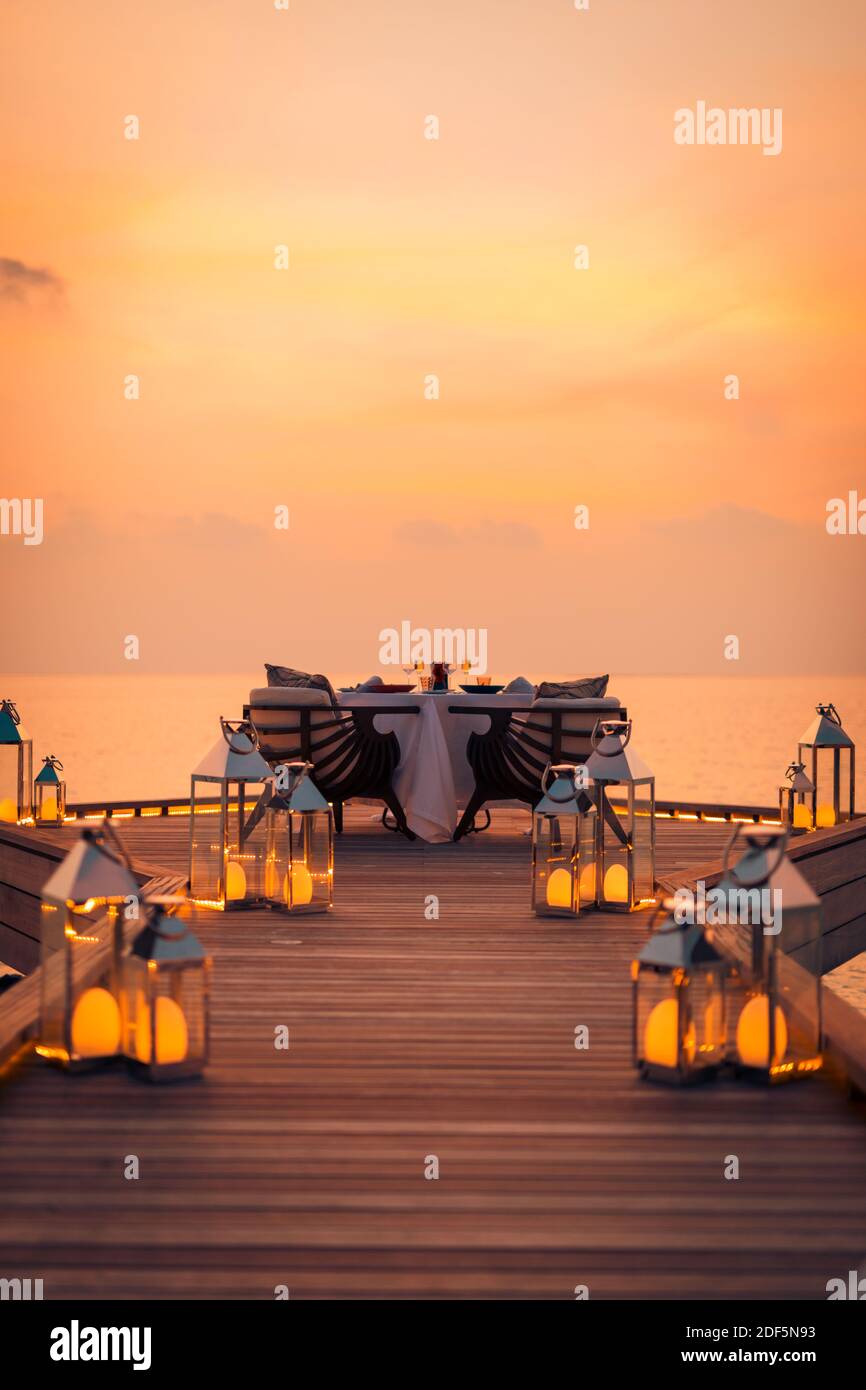 Toller romantischer Strand zum Abendessen auf einer Holzterrasse mit Kerzen unter dem Sonnenuntergang. Romantik Liebe, Luxus Destination Dining, exotische Tisch Setup, Meerblick Stockfoto