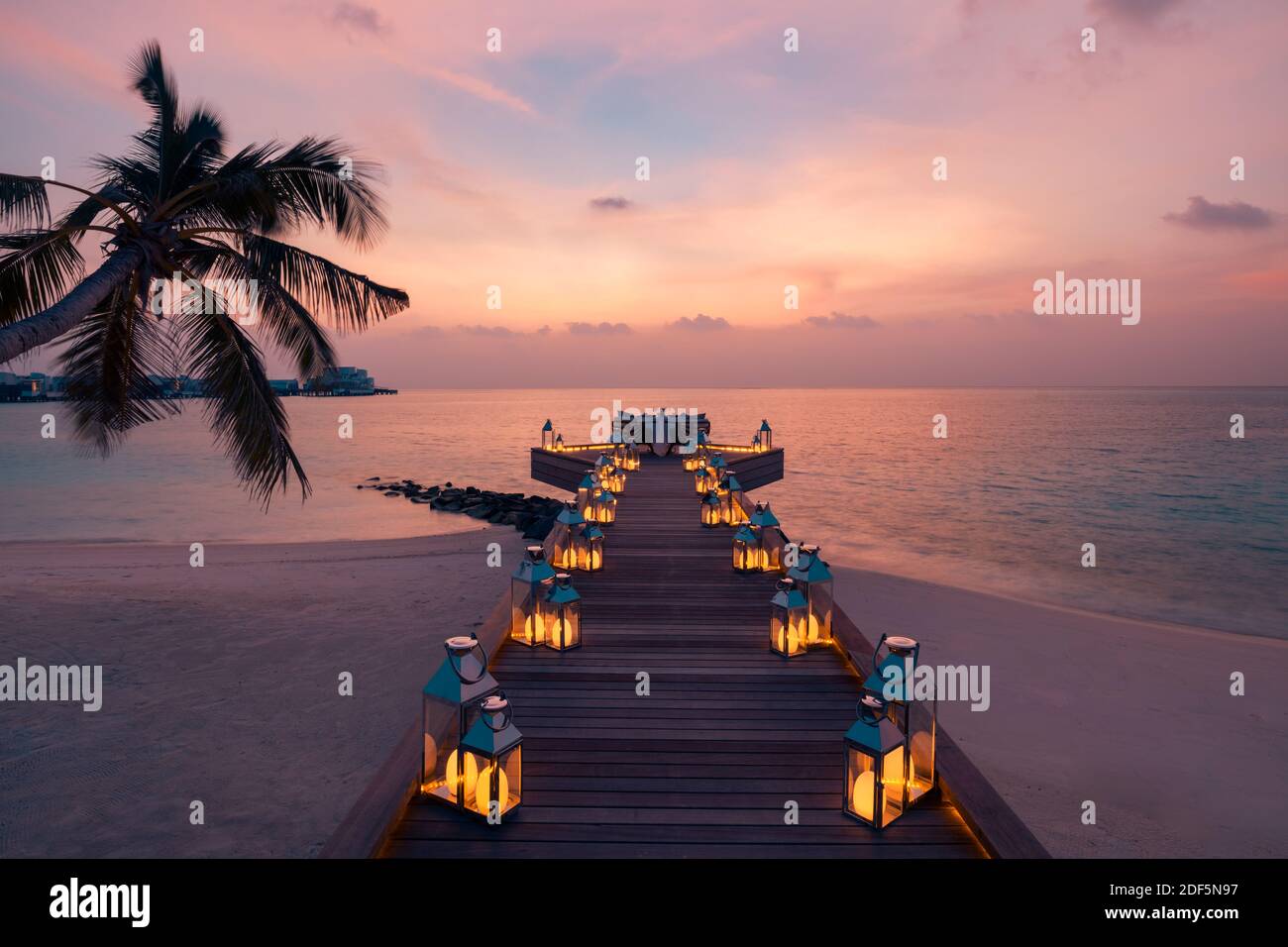 Toller romantischer Strand zum Abendessen auf einer Holzterrasse mit Kerzen unter dem Sonnenuntergang. Romantik Liebe, Luxus Destination Dining, exotische Tisch Setup, Meerblick Stockfoto