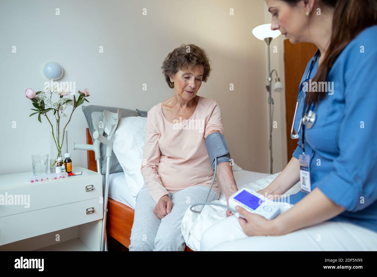 Home Caregiver Überprüfung des Blutdrucks von älteren Patienten sitzen auf Krankenhausbett. Home Care Krankenschwester, die den Blutdruck der älteren Frau. Stockfoto