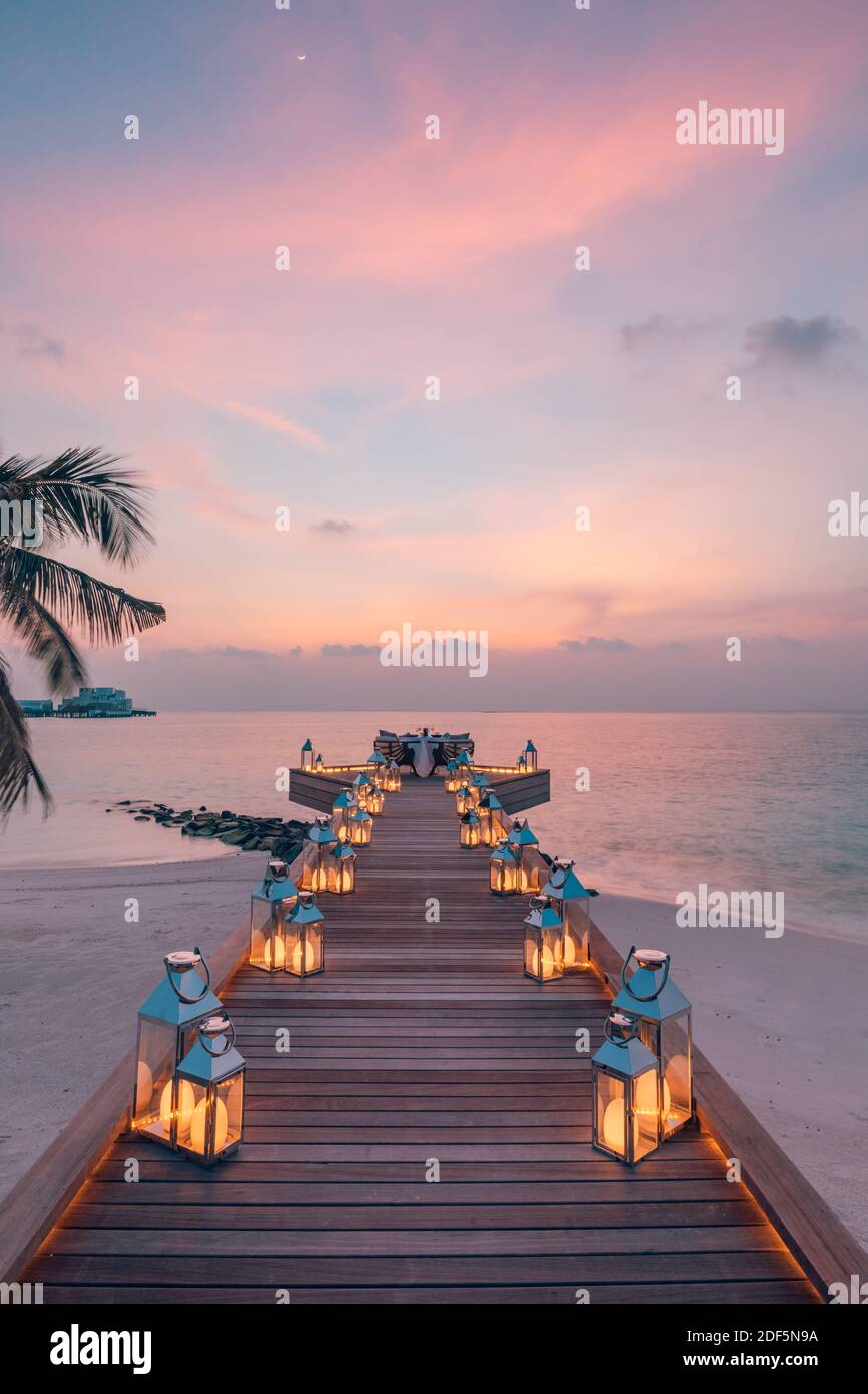Toller romantischer Strand zum Abendessen auf einer Holzterrasse mit Kerzen unter dem Sonnenuntergang. Romantik Liebe, Luxus Destination Dining, exotische Tisch Setup, Meerblick Stockfoto