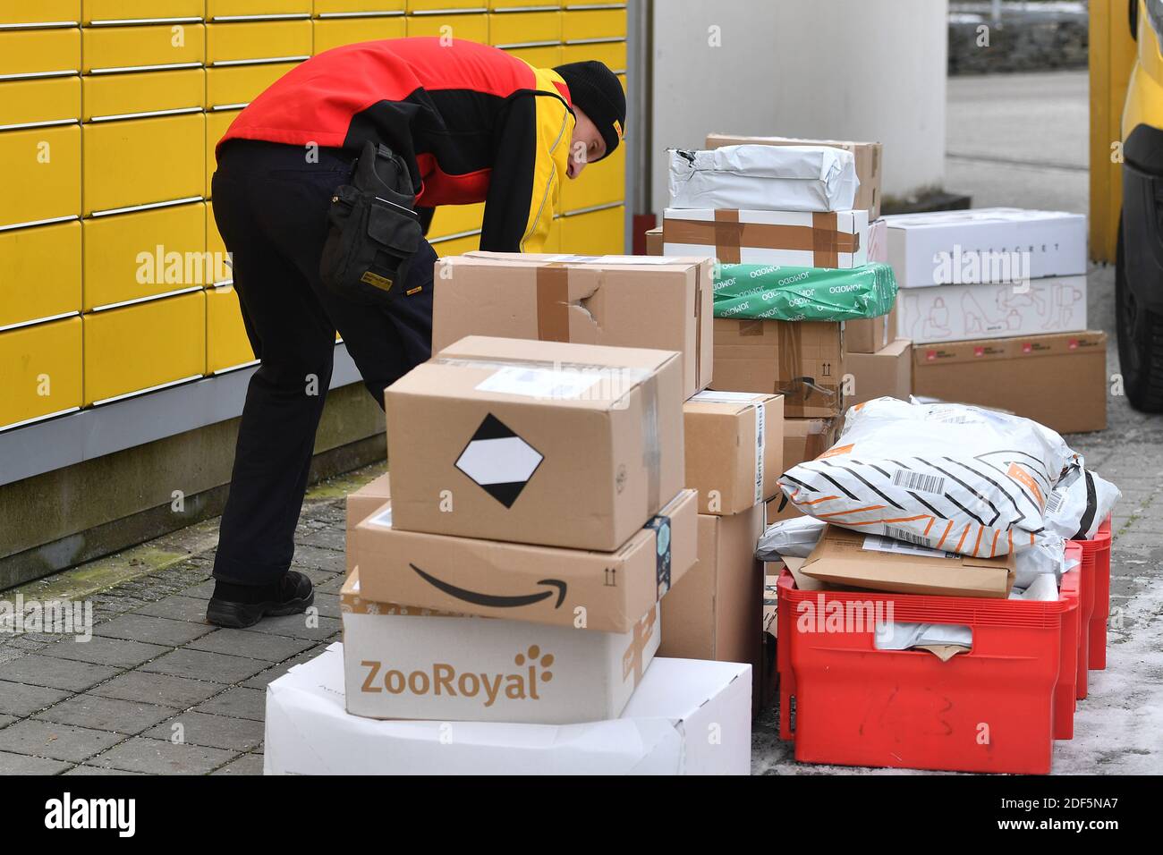 München, Deutschland. Dezember 2020. Paketvolumen und Online-Handel boomen in Zeiten der Corona-Virus-Pandemie. DHL Paketzusteller, Paketdienstleister, bei der Arbeit legt Paket in ein Fach einer Packstation. Entlädt seine Paket Auto, Postbus, DHL, Paket, Pakete, Paketdienst, liefern, liefern, entladen, Versand, Transporter, Handfahrzeug. Quelle: dpa/Alamy Live News Stockfoto