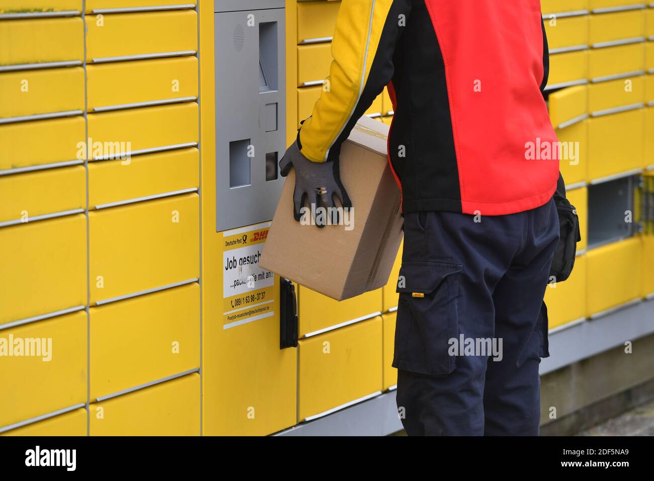 München, Deutschland. Dezember 2020. Paketvolumen und Online-Handel boomen in Zeiten der Corona-Virus-Pandemie. DHL Paketzusteller, Paketdienstleister, bei der Arbeit legt Paket in ein Fach einer Packstation. Entlädt seine Paket Auto, Postbus, DHL, Paket, Pakete, Paketdienst, liefern, liefern, entladen, Versand, Transporter, Handfahrzeug. Quelle: dpa/Alamy Live News Stockfoto