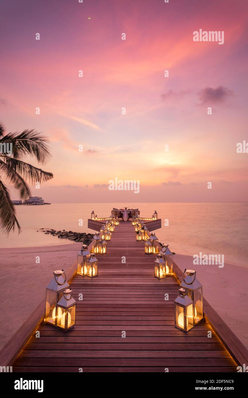 Toller romantischer Strand zum Abendessen auf einer Holzterrasse mit Kerzen unter dem Sonnenuntergang. Romantik Liebe, Luxus Destination Dining, exotische Tisch Setup, Meerblick Stockfoto