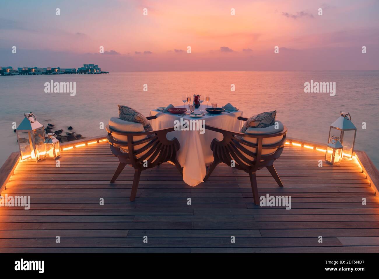 Toller romantischer Strand zum Abendessen auf einer Holzterrasse mit Kerzen unter dem Sonnenuntergang. Romantik Liebe, Luxus Destination Dining, exotische Tisch Setup, Meerblick Stockfoto