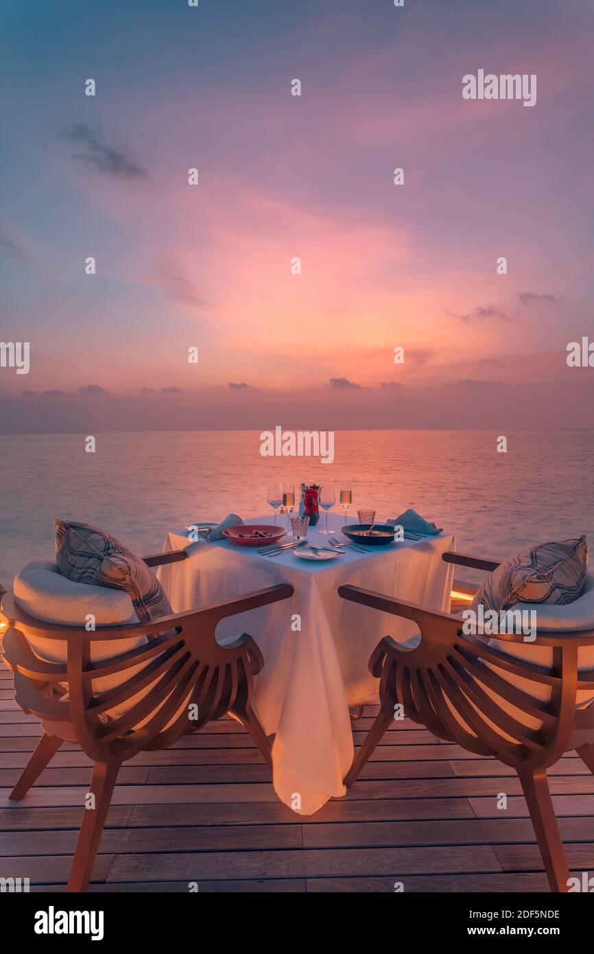 Toller romantischer Strand zum Abendessen auf einer Holzterrasse mit Kerzen unter dem Sonnenuntergang. Romantik Liebe, Luxus Destination Dining, exotische Tisch Setup, Meerblick Stockfoto