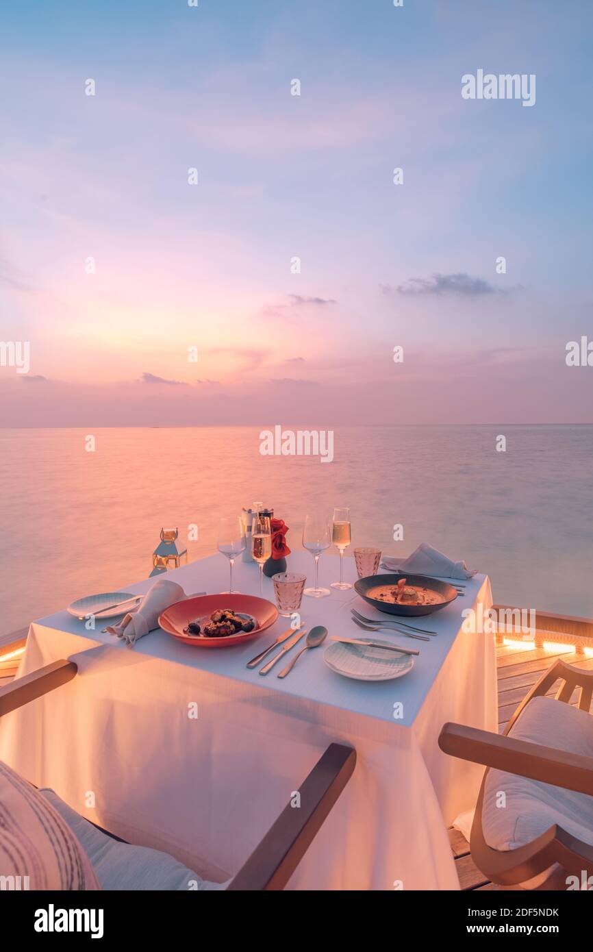 Toller romantischer Strand zum Abendessen auf einer Holzterrasse mit Kerzen unter dem Sonnenuntergang. Romantik Liebe, Luxus Destination Dining, exotische Tisch Setup, Meerblick Stockfoto