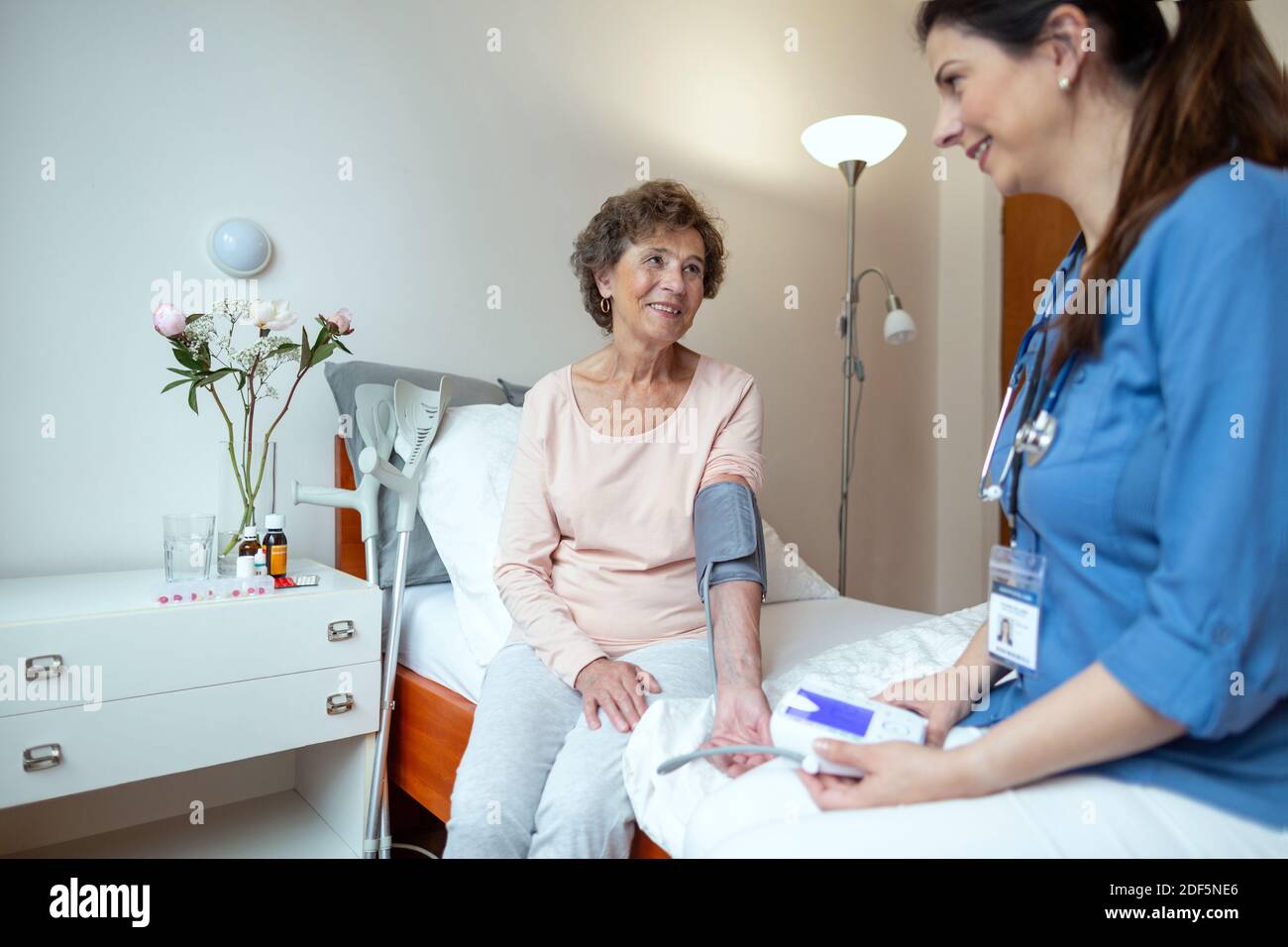 Ältere Frau lächelt an Home Caregiver, die ihren Blutdruck im Schlafzimmer nimmt. Pflege Krankenschwester Überprüfung des Blutdrucks der älteren Frau. Stockfoto