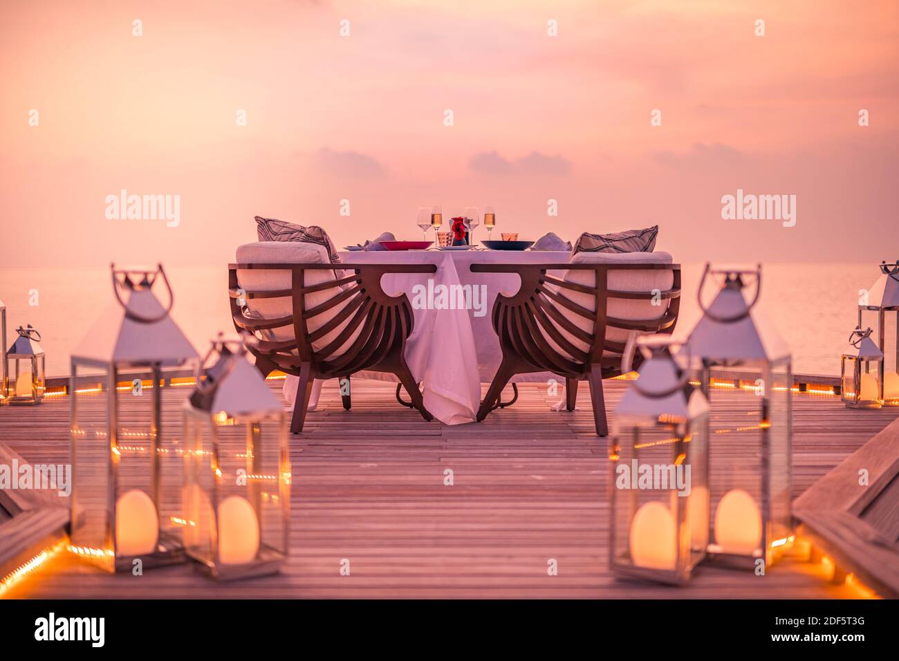 Tolles romantisches Abendessen am Strand auf der Holzterrasse mit Kerzen unter dem Sonnenuntergangshimmel. Romantik und Liebe, Luxus-Destination Dining, exotische Tisch-Setup Stockfoto
