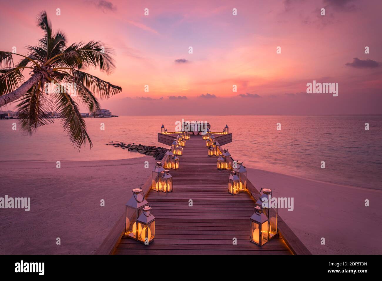 Tolles romantisches Abendessen am Strand auf der Holzterrasse mit Kerzen unter dem Sonnenuntergangshimmel. Romantik und Liebe, Luxus-Destination Dining, exotische Tisch-Setup Stockfoto