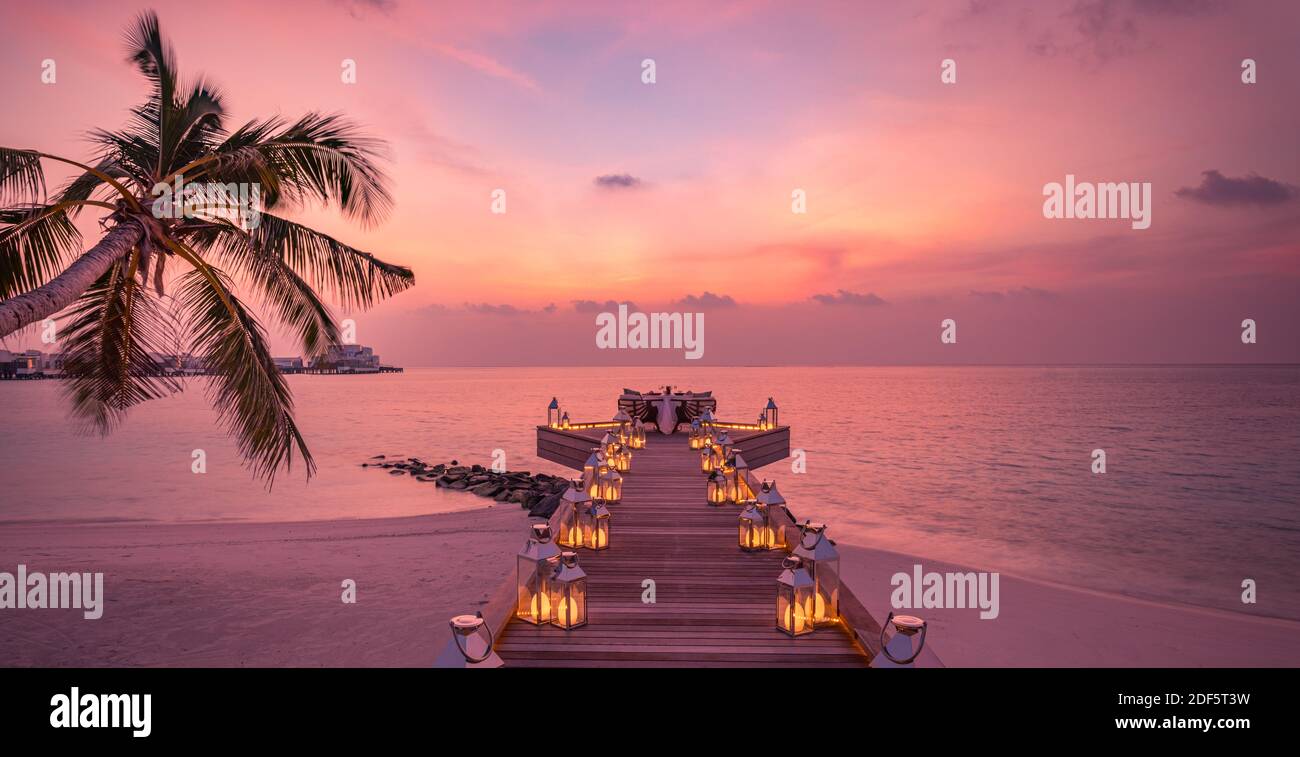 Tolles romantisches Abendessen am Strand auf der Holzterrasse mit Kerzen unter dem Sonnenuntergangshimmel. Romantik und Liebe, Luxus-Destination Dining, exotische Tisch-Setup Stockfoto