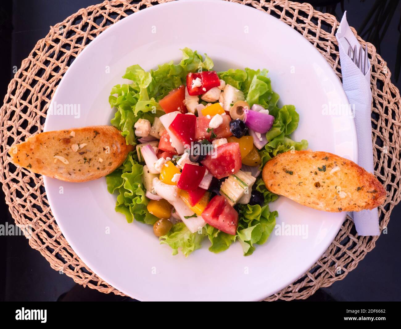 Weißer Teller mit griechischem Salat und zwei Scheiben Knoblauchbrot. Stockfoto