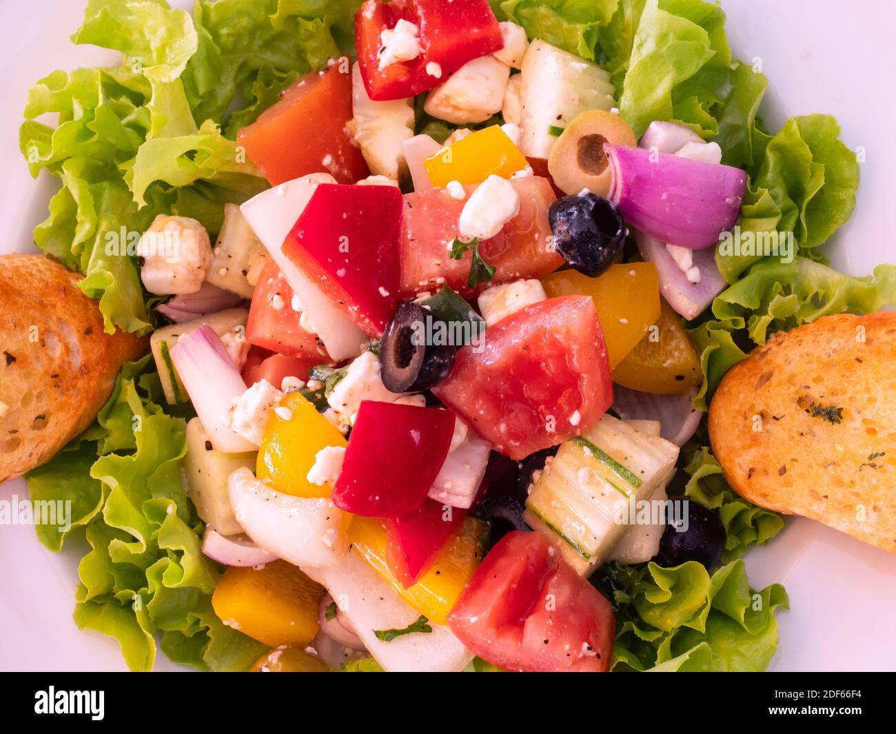 Weißer Teller mit griechischem Salat und zwei Scheiben Knoblauchbrot. Stockfoto