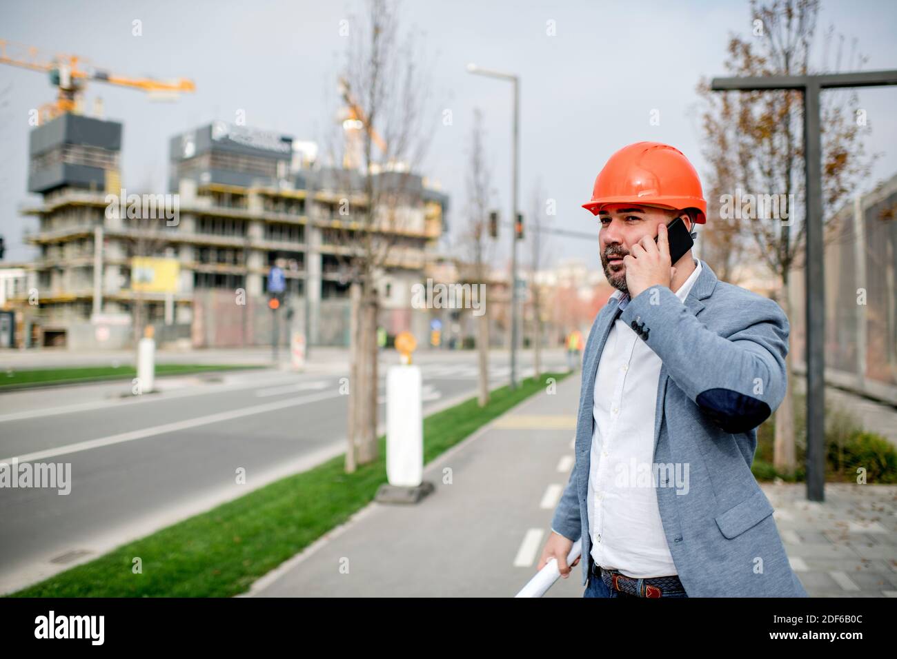 Junger Architekt hält Handy und Blaupause, während er wegschaut. Stockfoto