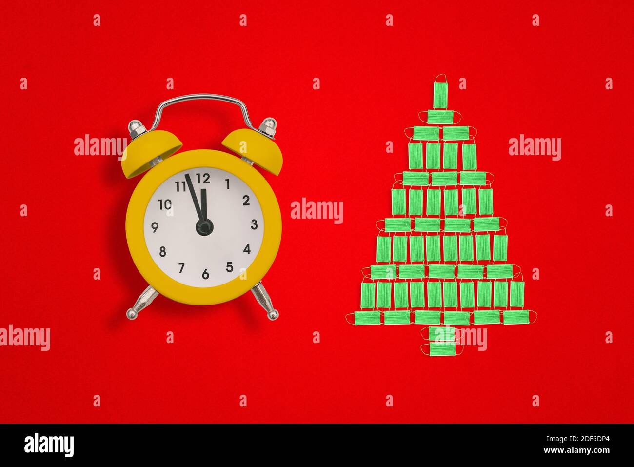 Weihnachtsbaum aus medizinischen Gesichtsmasken und Wecker auf rotem Hintergrund. Die Zeiger der Uhr zeigen zwölf Uhr. Weihnachtsidee. Stockfoto