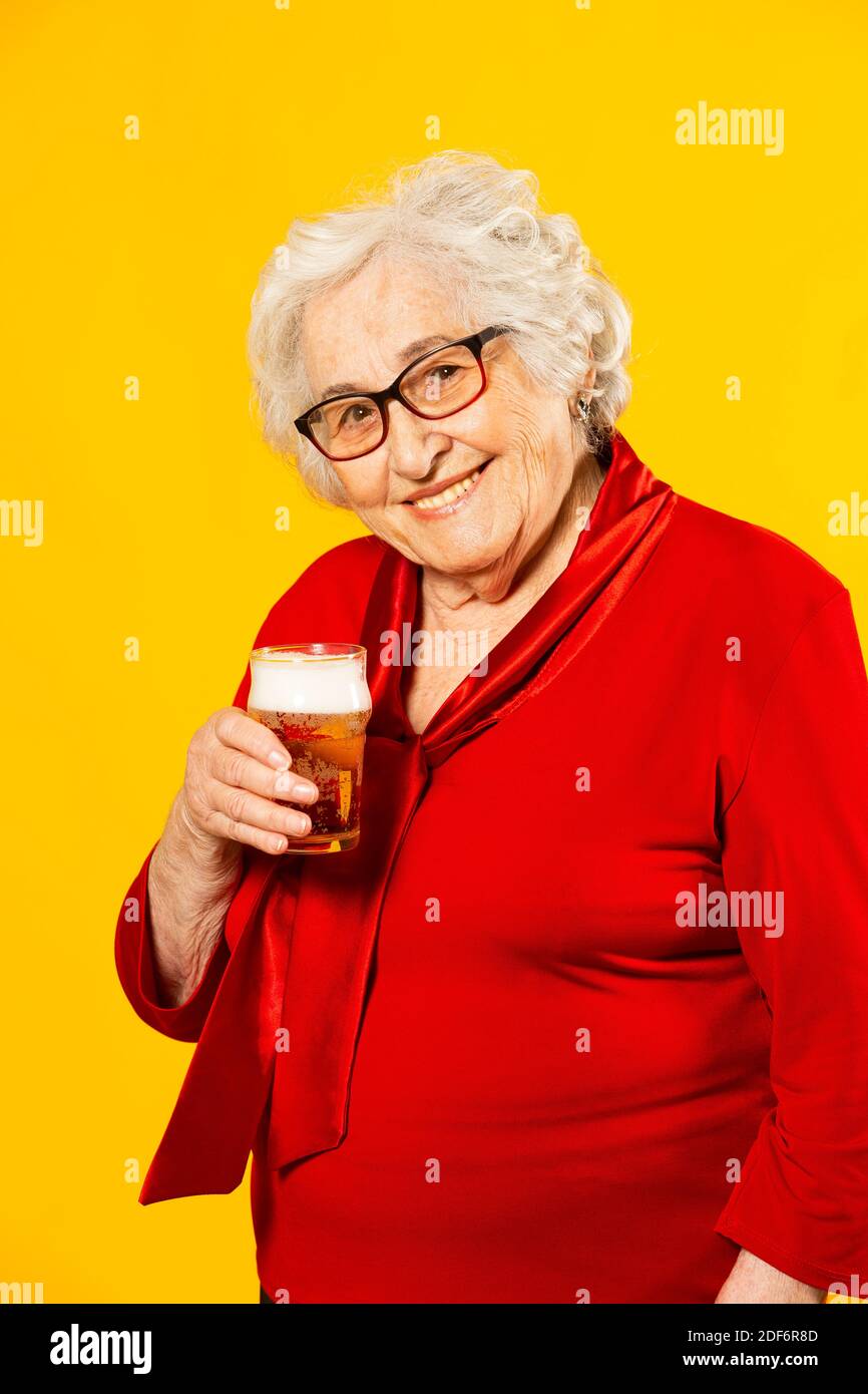 Studioportrait einer älteren Frau in einem roten Hemd mit einem Glas Bier auf einem gelben Hintergrund Stockfoto