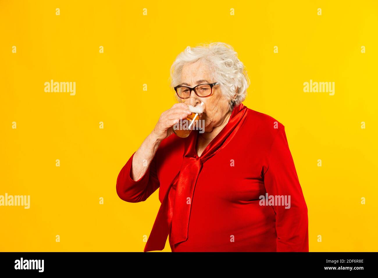 Studio Porträt einer älteren Frau trägt rotes Hemd trinken Von einem halben Pint Bier gegen ein Gelb Hintergrund Stockfoto