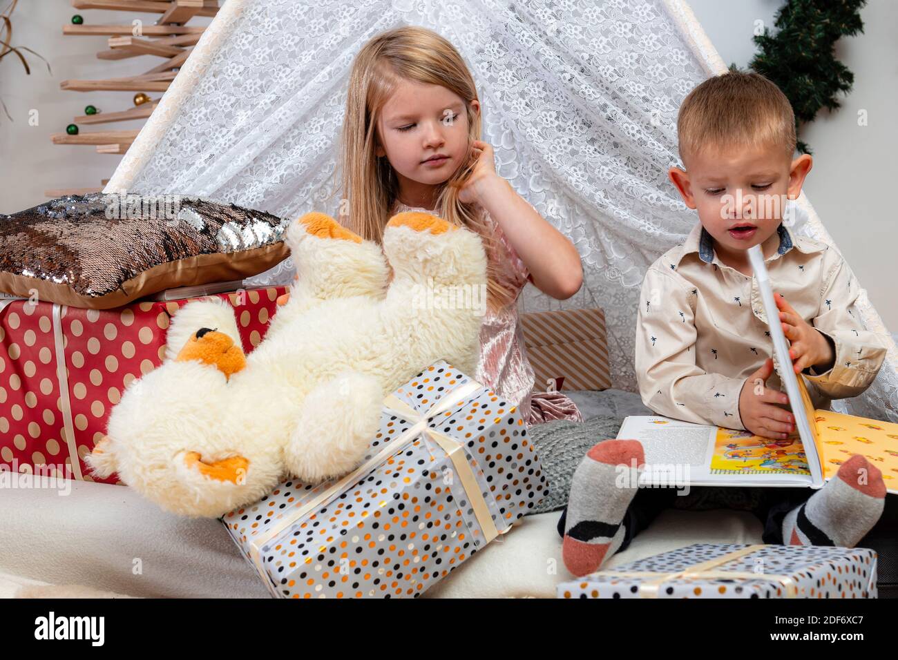 Glückliche Kinder sitzen zwischen Weihnachtsgeschenkschachteln und Spielzeug und Lesen eines Buches Stockfoto