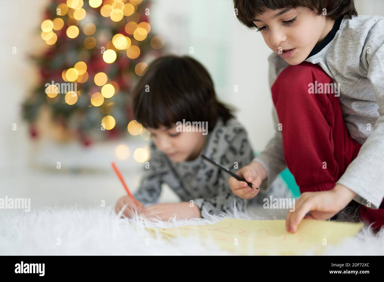Nahaufnahme von zwei kleinen lateinischen Jungen, Zwillinge zeichnen, während auf dem Boden zu Hause sitzen dekoriert für Weihnachten. Kindheit, Familie, Winterurlaub Konzept Stockfoto