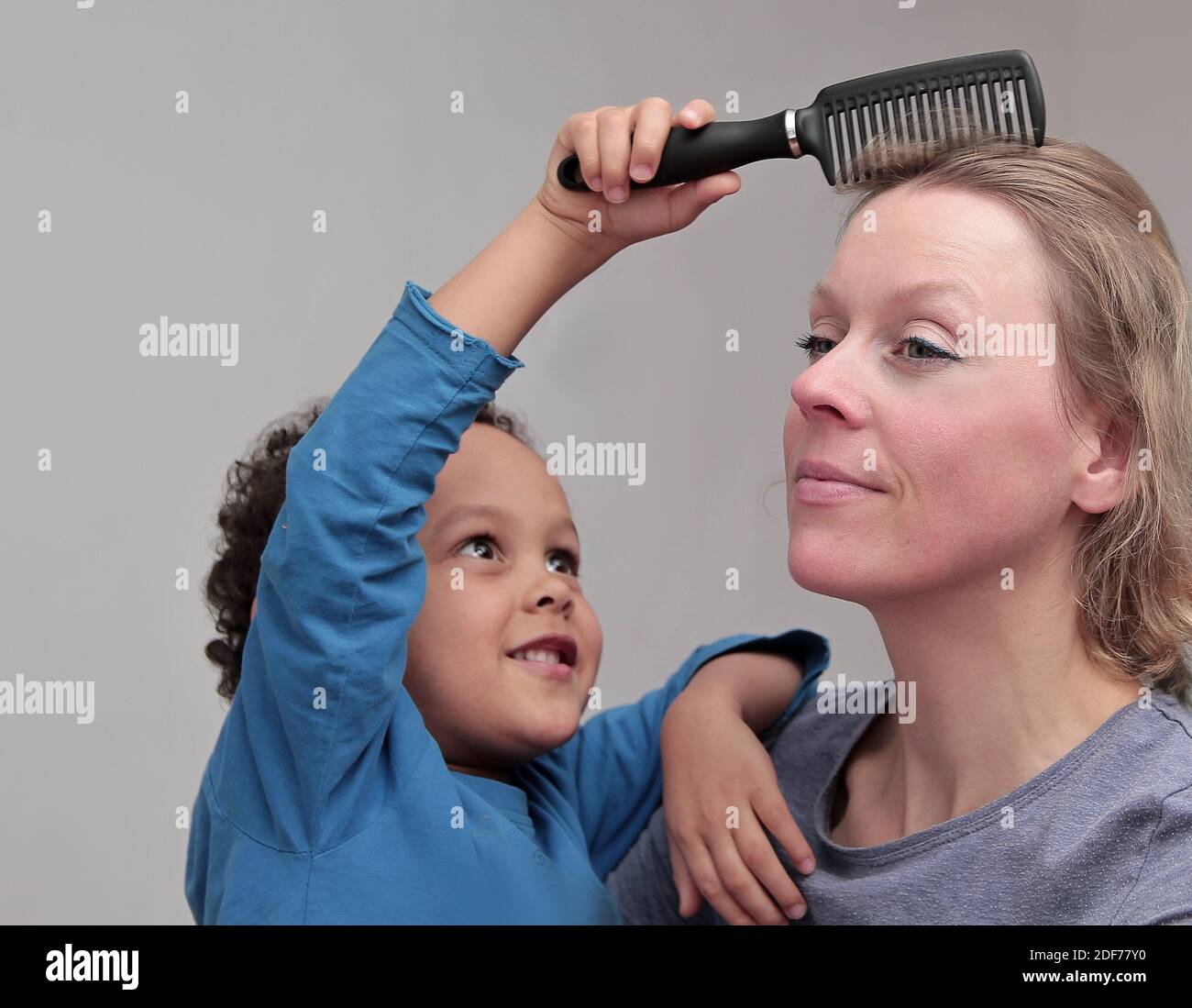 Kind spielt Friseur mit Mutter auf grauem Hintergrund Stock Foto Stockfoto
