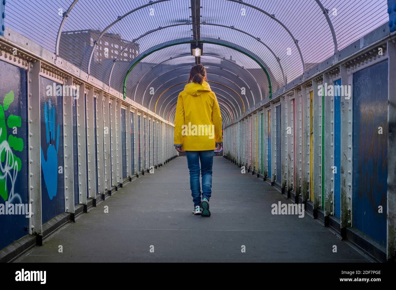 Frau, die über eine Brücke geht und einen gelben Mantel trägt, Rückansicht. Stockfoto