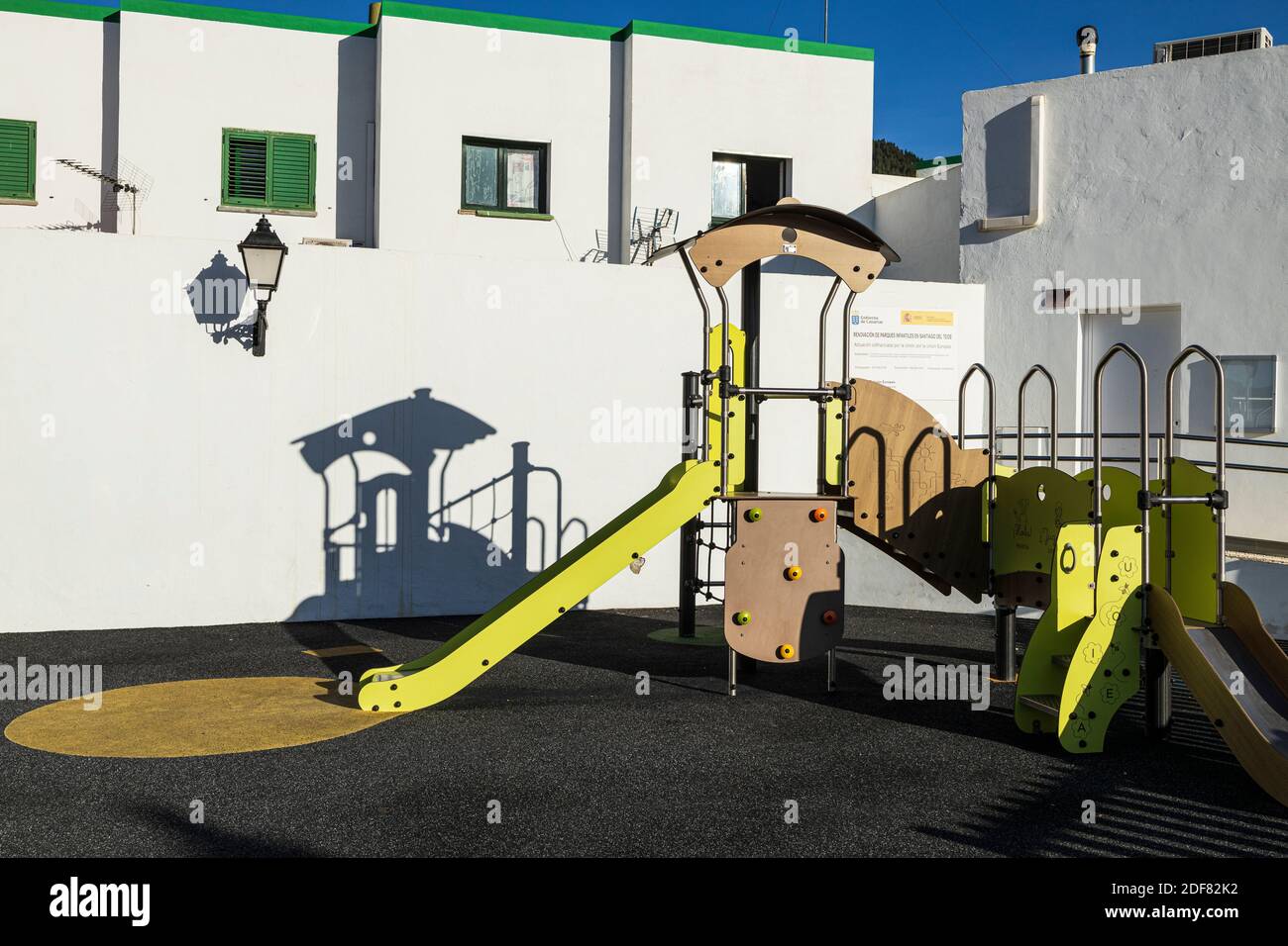 Kinderspielplatz Rutsche und Klettergerüst wirft trainähnlichen Schatten an Wand des Wohnblocks in Santiago del Teide, Teneriffa, Kanarische Inseln, Spai Stockfoto