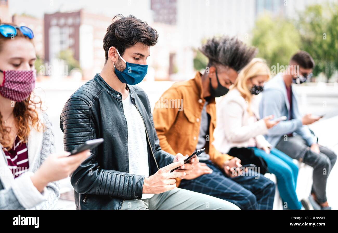 Multirassische Freunde, die Mobiltelefone verwenden, die mit einer Gesichtsmaske bedeckt sind Covid zweite Welle - besorgt Jungs und Mädchen Nachrichten beobachten Auf Smartphone-Geräten Stockfoto