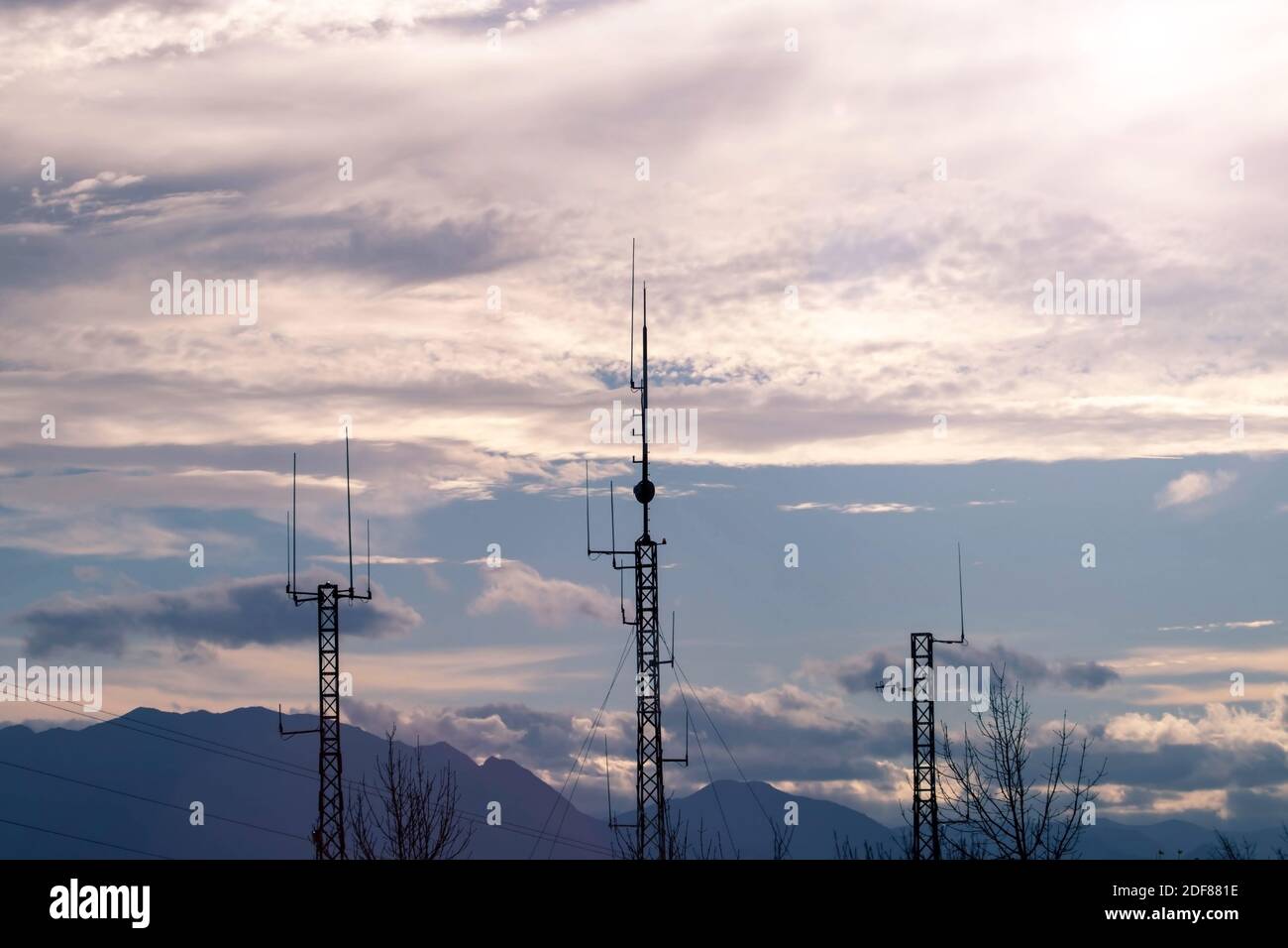 Drei Telekommunikationsmasten oder mobile Türme mit Satellitenantennen Silhouetten bei Sonnenuntergang cludy Himmel Hintergrund. Stockfoto