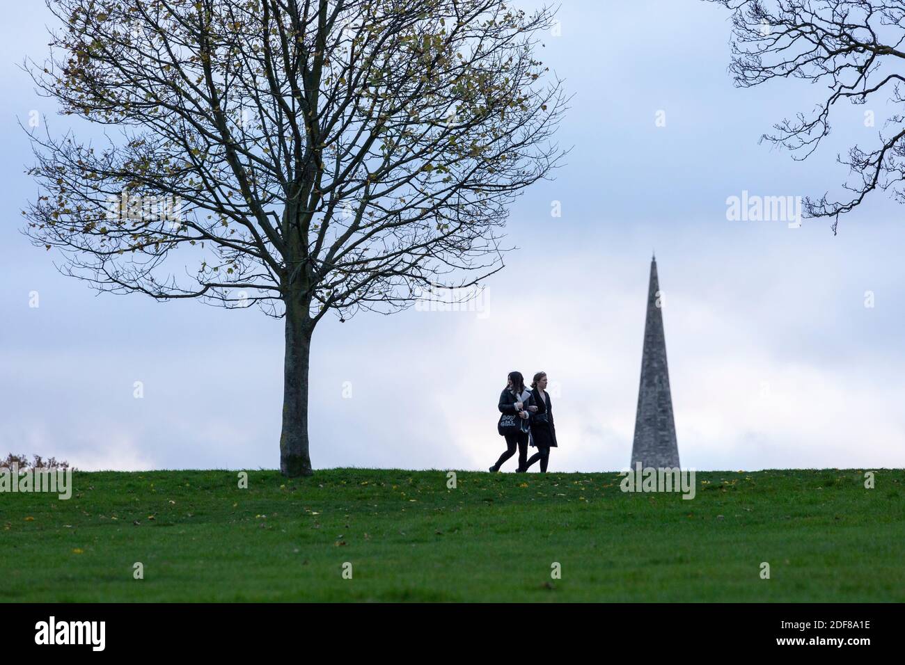 Zwei Mädchen gehen im Brockwell Park mit dem Kirchturm der Holy Trinity Church im Hintergrund, London Stockfoto