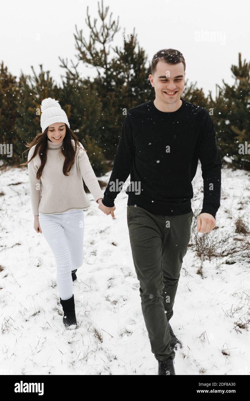 Junger Mann und Frau gehen im Kiefernwald auf den Schnee und halten sich die Hände. Liebe, Beziehung, Winterurlaub. Winter paar Foto-Ideen Stockfoto